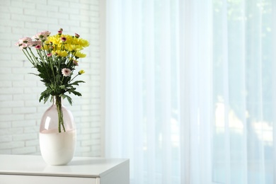 Photo of Vase with beautiful flowers on table near window indoors, space for text. Stylish element of interior design