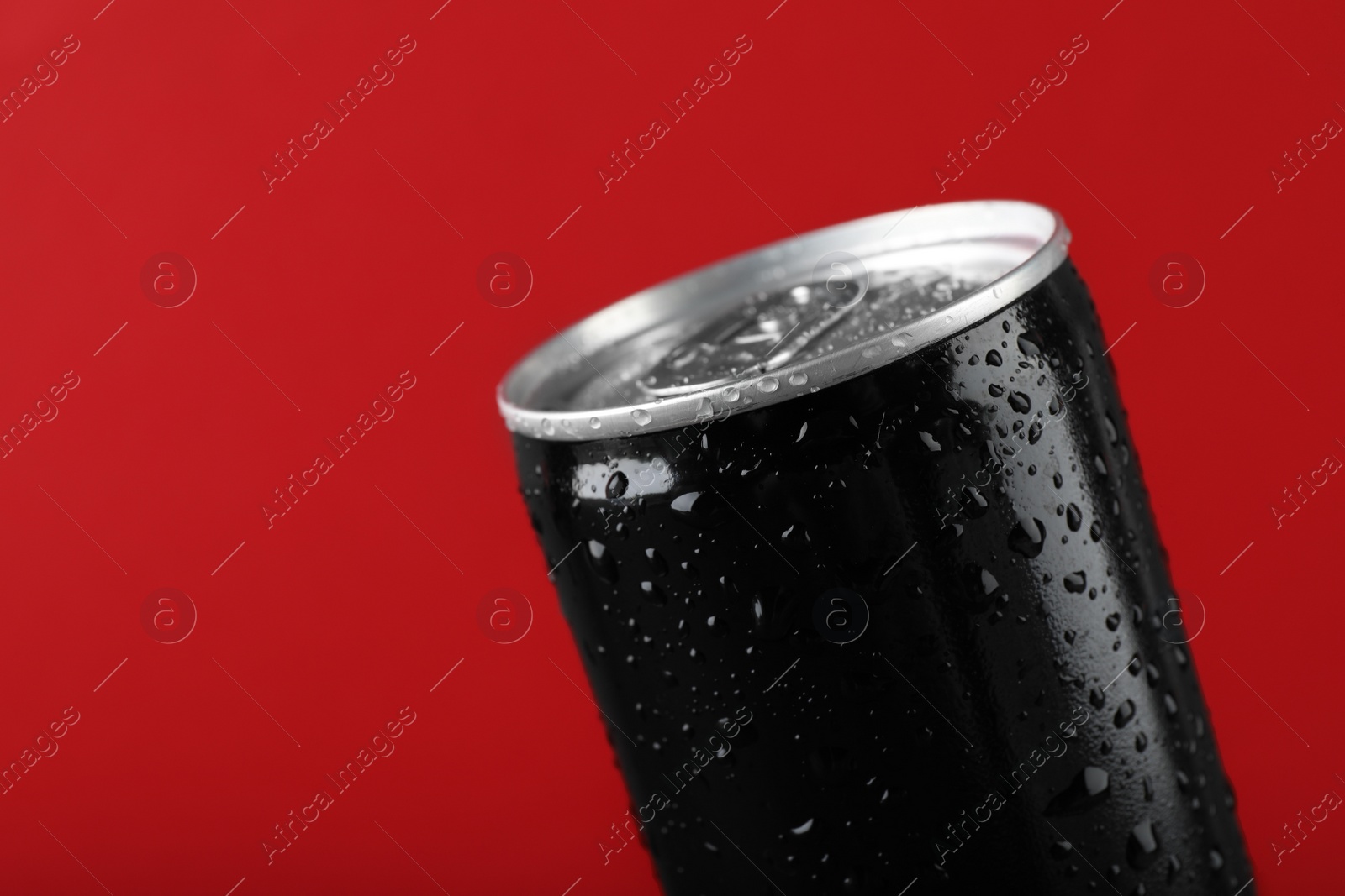 Photo of Black can of energy drink with water drops on red background, closeup. Space for text