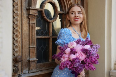 Beautiful woman with bouquet of spring flowers near building outdoors, space for text