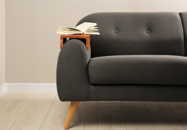 Open book on sofa with wooden armrest table in room. Interior element