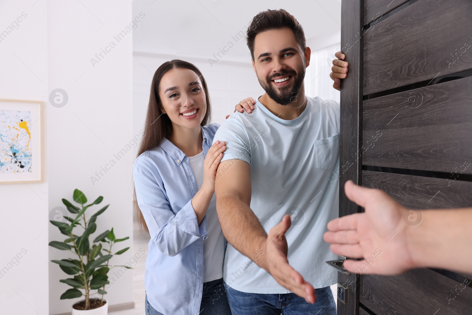 Photo of Happy couple welcoming their guest near door. Invitation to come indoors