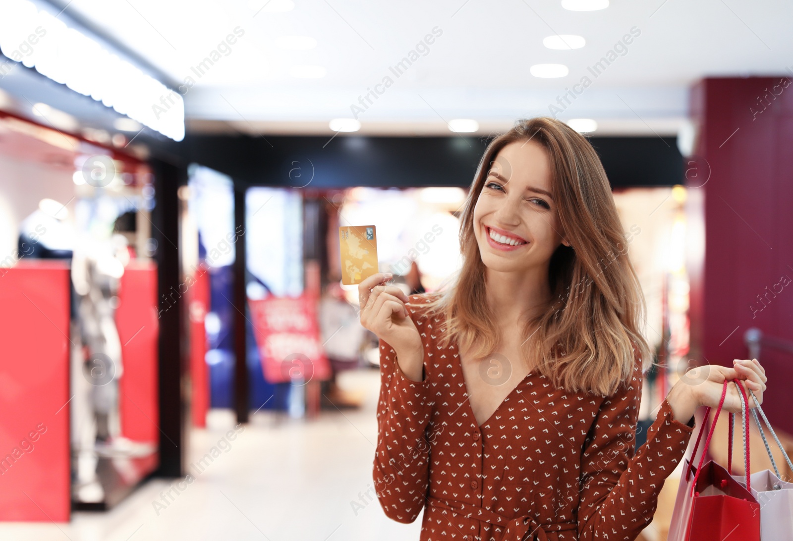 Photo of Happy young woman with shopping bags and credit card in mall