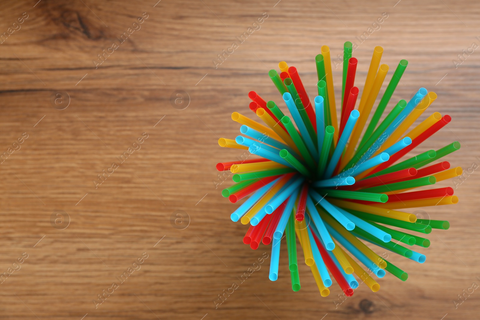 Photo of Colorful plastic drinking straws on wooden table, top view. Space for text