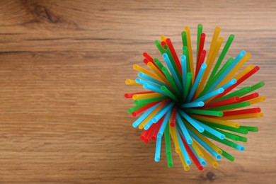 Photo of Colorful plastic drinking straws on wooden table, top view. Space for text