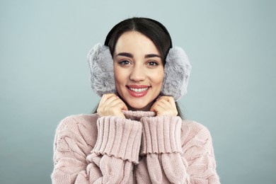 Photo of Beautiful young woman wearing earmuffs on light grey background