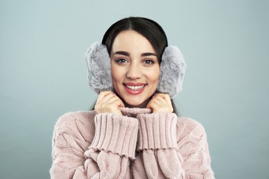 Beautiful young woman wearing earmuffs on light grey background