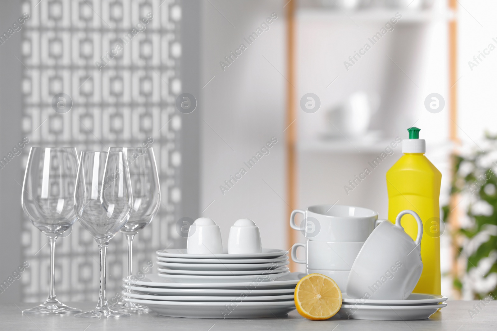 Photo of Clean dishware, glasses and bottle of detergent on light grey table