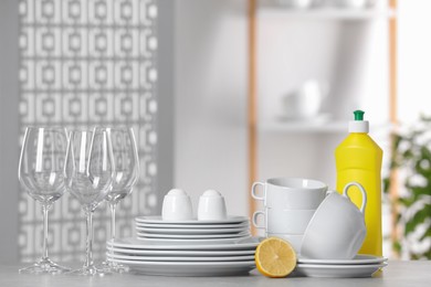 Clean dishware, glasses and bottle of detergent on light grey table