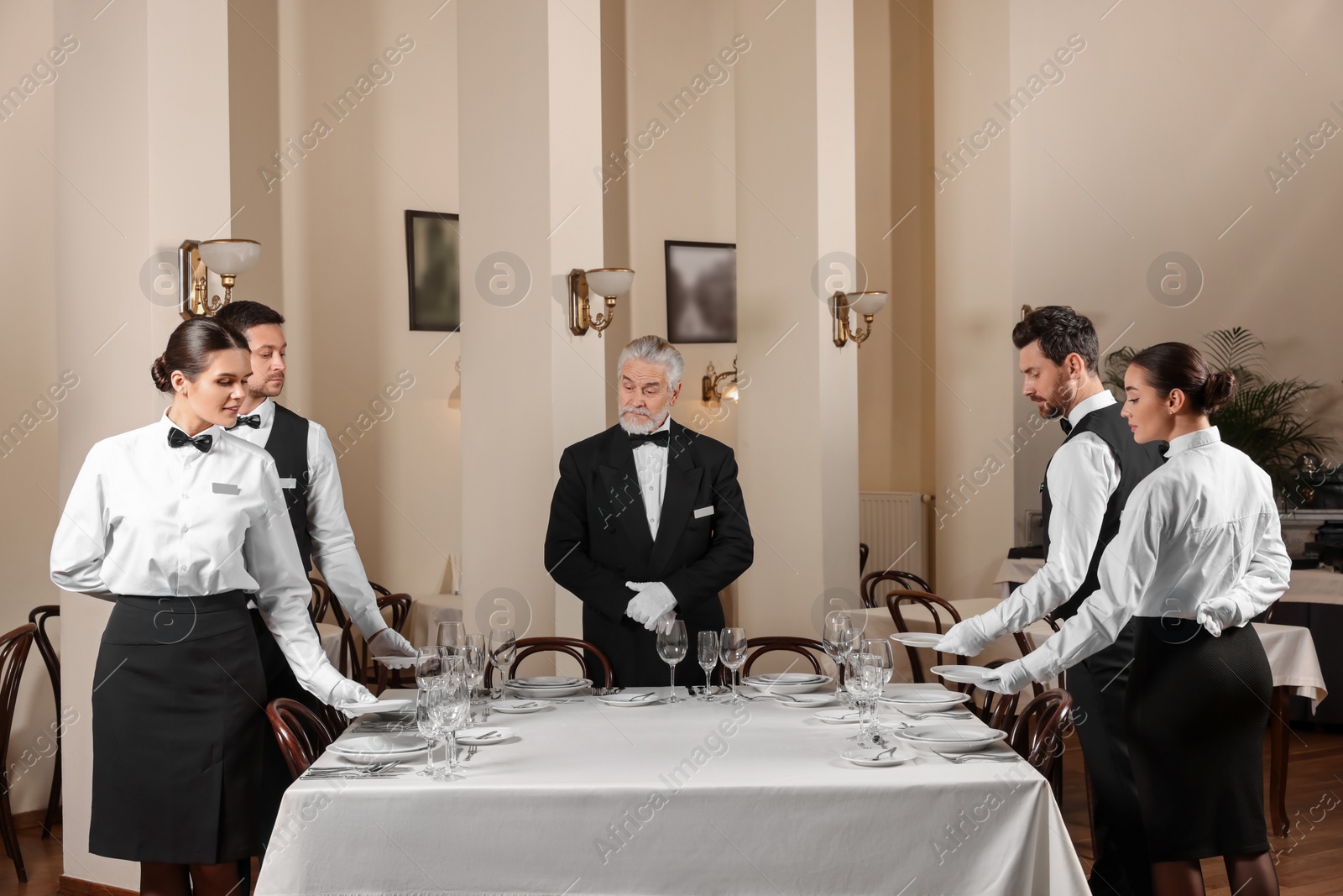 Photo of Senior man wearing formal suit teaching trainees in restaurant. Professional butler courses