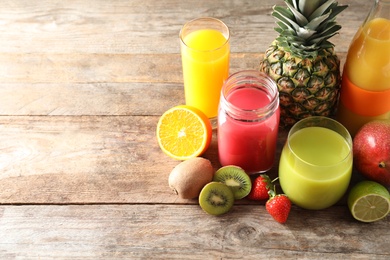 Photo of Glassware with different juices and fresh fruits on wooden background. Space for text