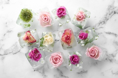 Ice cubes with flowers on marble background, flat lay