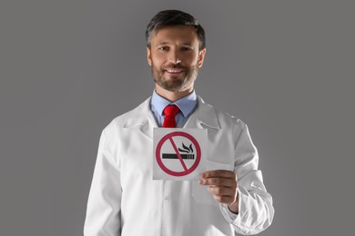 Doctor holding card with no smoking sign on gray background, selective focus