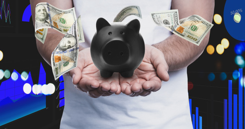 Young man holding piggy bank and American dollars falling on color background, closeup 