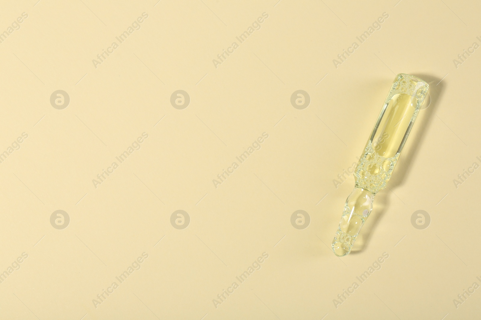 Photo of Glass ampoule with liquid on beige background, top view. Space for text