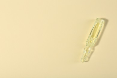 Photo of Glass ampoule with liquid on beige background, top view. Space for text