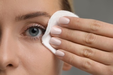 Photo of Woman removing makeup with cotton pad on grey background, closeup