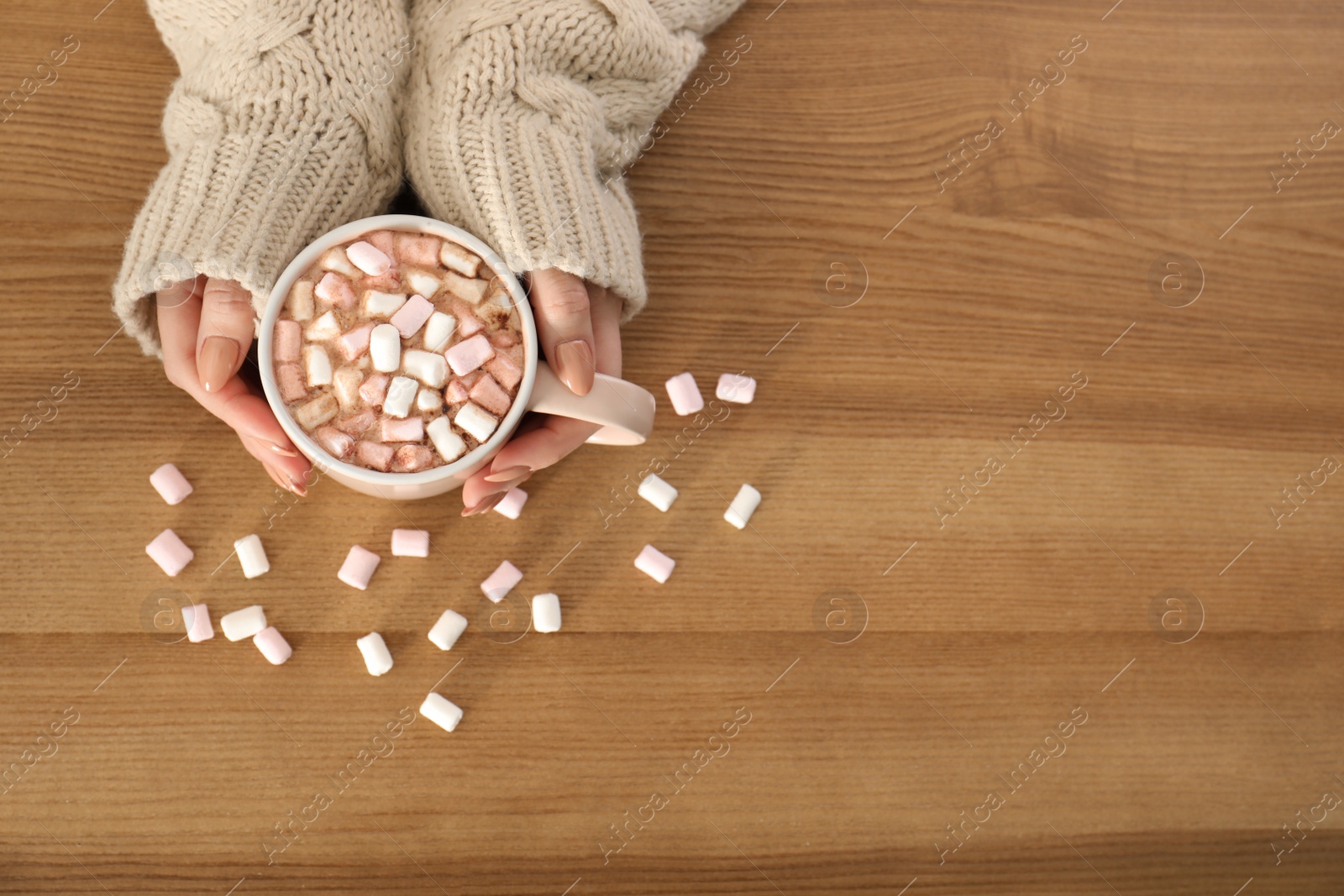 Photo of Woman holding cup of aromatic cacao with marshmallows on wooden background, top view. Space for text