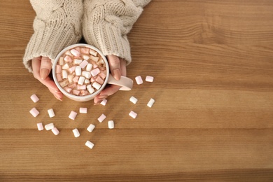 Photo of Woman holding cup of aromatic cacao with marshmallows on wooden background, top view. Space for text