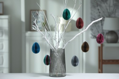 Branches with paper eggs in vase on white table at home. Beautiful Easter decor