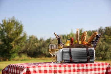 Photo of Picnic basket with wine, snacks and mat on table in park. Space for text