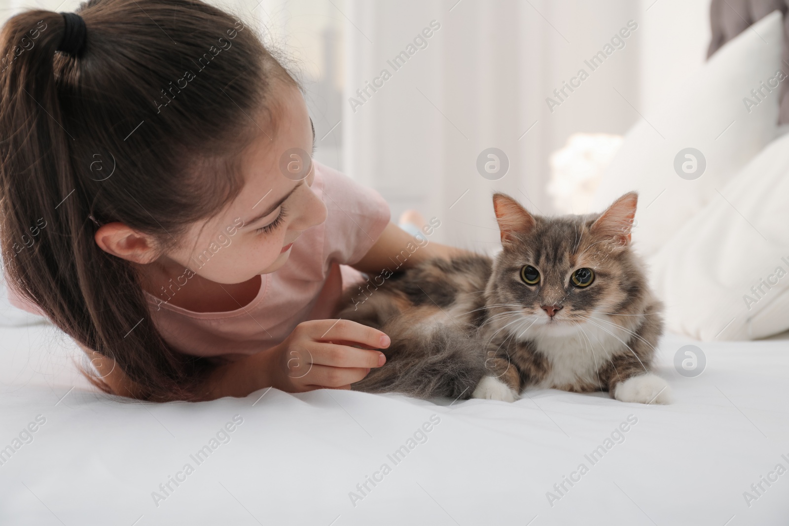 Photo of Cute little girl with cat lying on bed at home. First pet