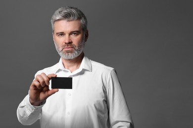 Photo of Handsome man holding blank business card on grey background. Space for text