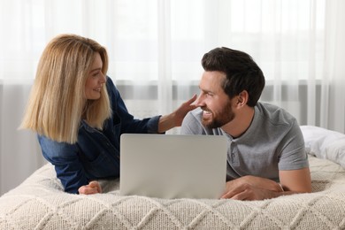 Happy couple with laptop on bed at home