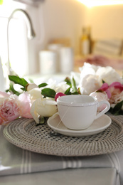 Photo of Beautiful peonies and cup of tea on kitchen counter