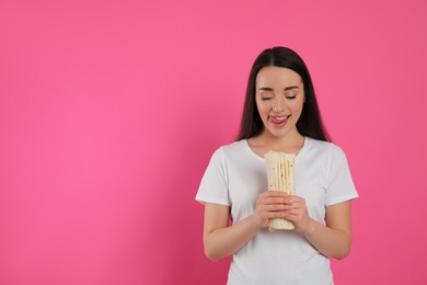 Happy young woman holding tasty shawarma on pink background. Space for text