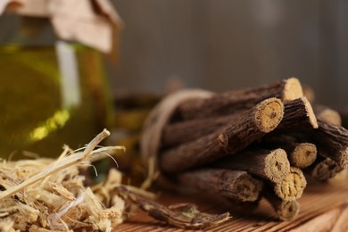 Photo of Dried sticks of licorice root and essential oil on wooden table, closeup