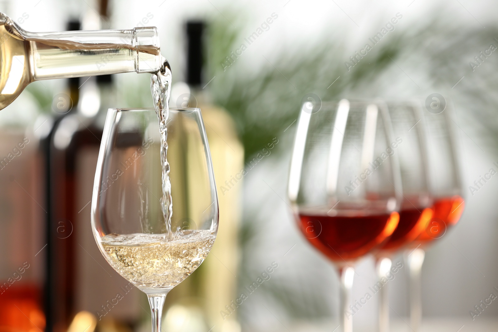 Photo of Pouring white wine from bottle into glass on blurred background, closeup. Space for text