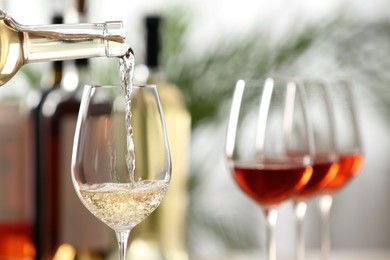 Photo of Pouring white wine from bottle into glass on blurred background, closeup. Space for text