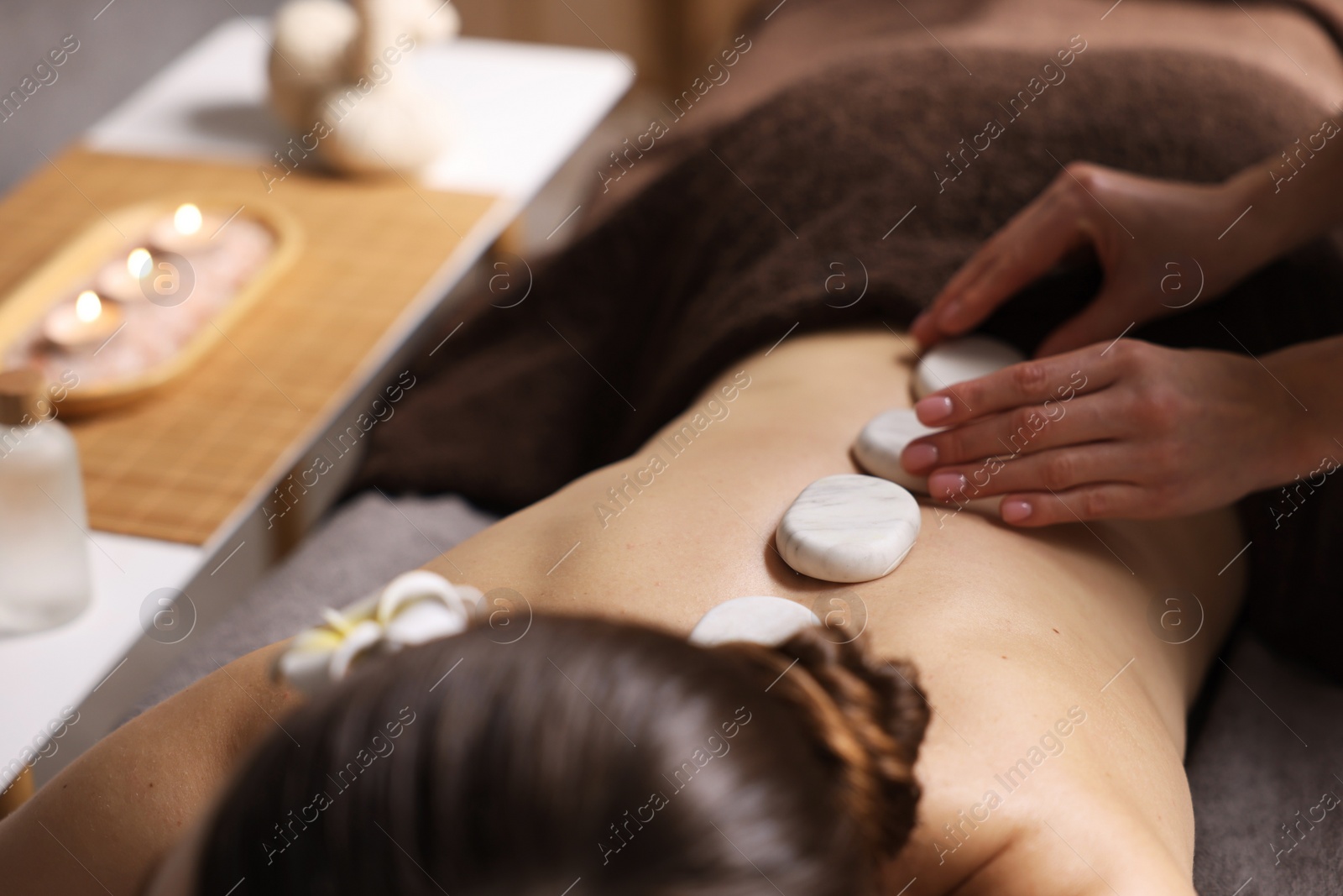 Photo of Spa therapy. Beautiful young woman lying on table during hot stone massage in salon, closeup