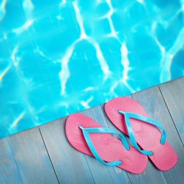 Image of Pair of flip flops on wooden deck near swimming pool, top view  