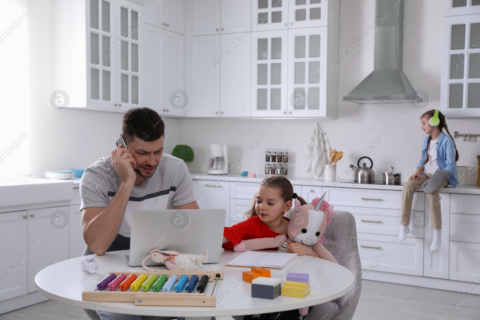 Photo of Children disturbing stressed man in kitchen. Working from home during quarantine