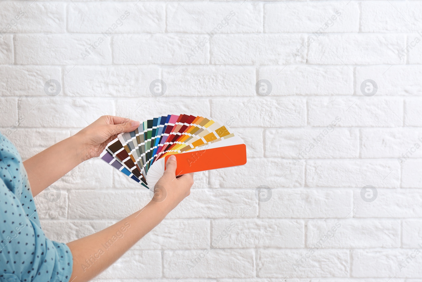 Photo of Female interior designer with color palette samples near brick wall, closeup. Space for text