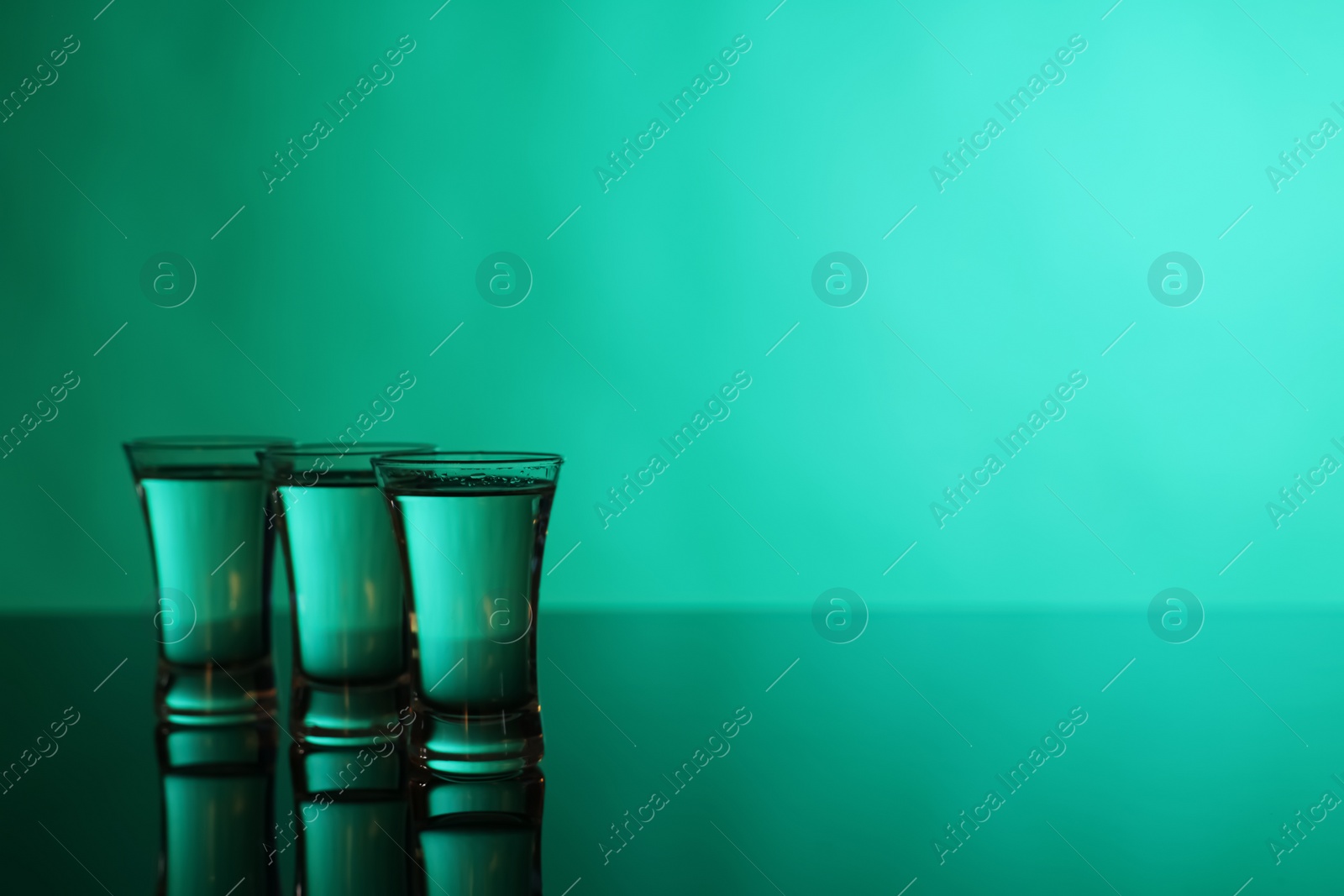 Photo of Vodka in shot glasses on green background, space for text