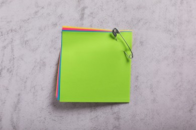 Colorful paper notes attached with safety pin on grey textured background, top view