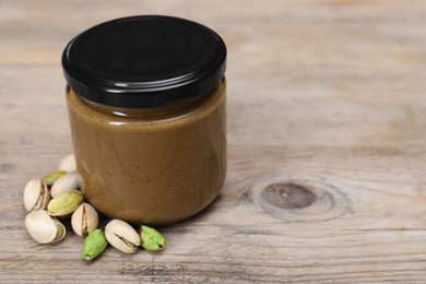 Tasty nut paste in jar and pistachios on wooden table, closeup. Space for text