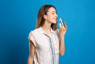 Photo of Young woman drinking lemon water on light blue background