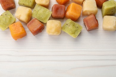 Photo of Different frozen fruit puree cubes on white wooden table, flat lay. Space for text