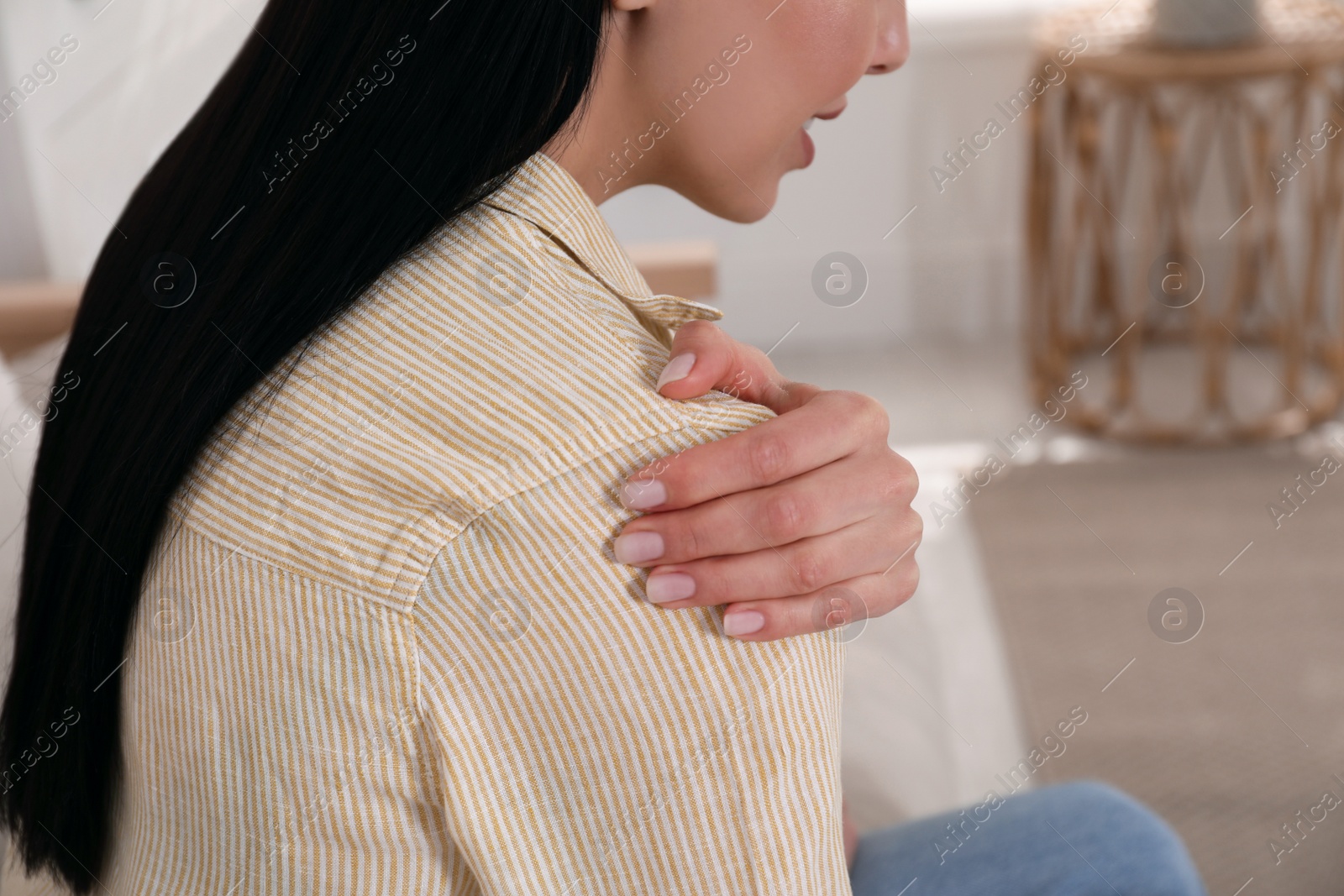 Photo of Woman suffering from shoulder pain at home, closeup