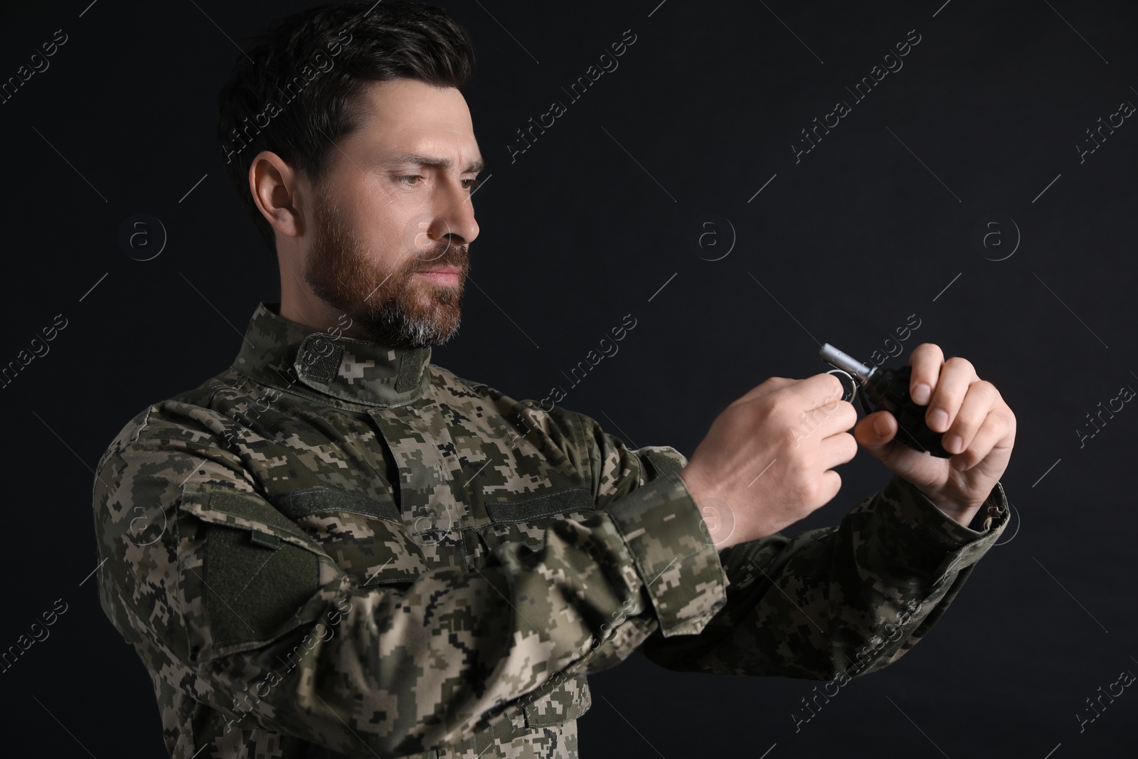 Photo of Soldier pulling safety pin out of hand grenade on black background. Military service