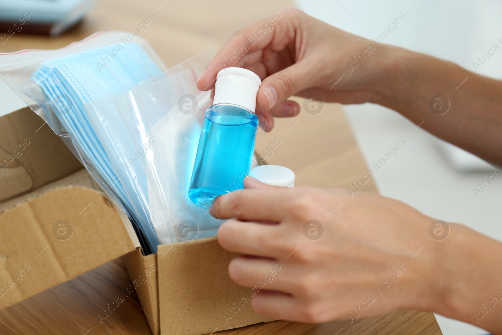 Photo of Woman unpacking box with antiseptics and respiratory masks at wooden table, closeup. Protective essentials during COVID-19 pandemic
