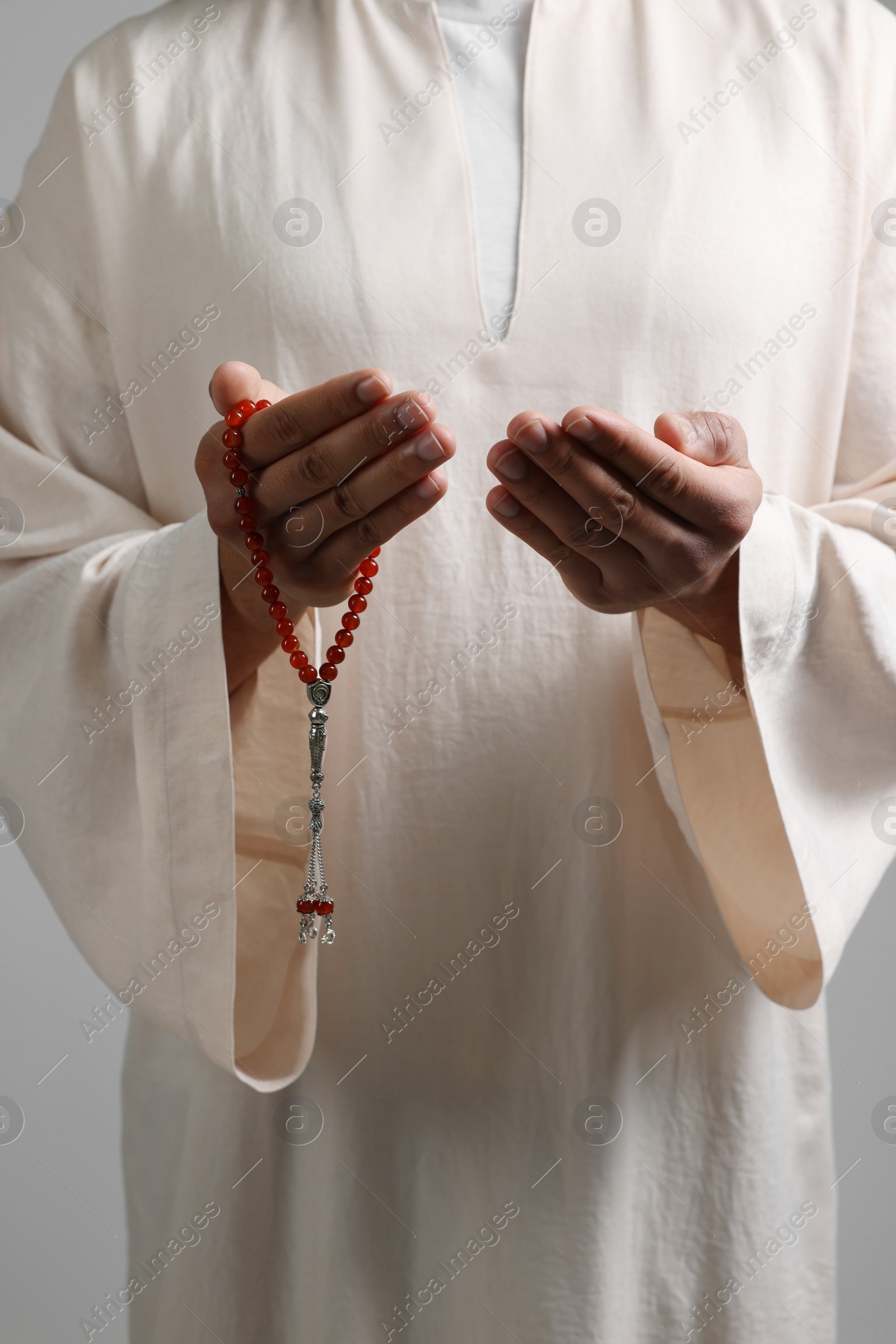 Photo of Muslim man with misbaha praying on light grey background, closeup