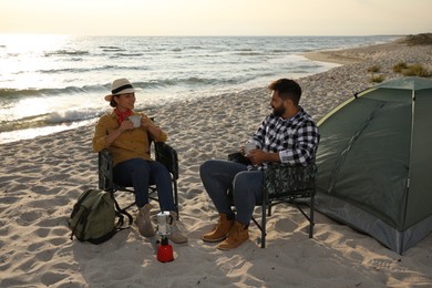 Photo of Couple with hot drinks near camping tent on beach