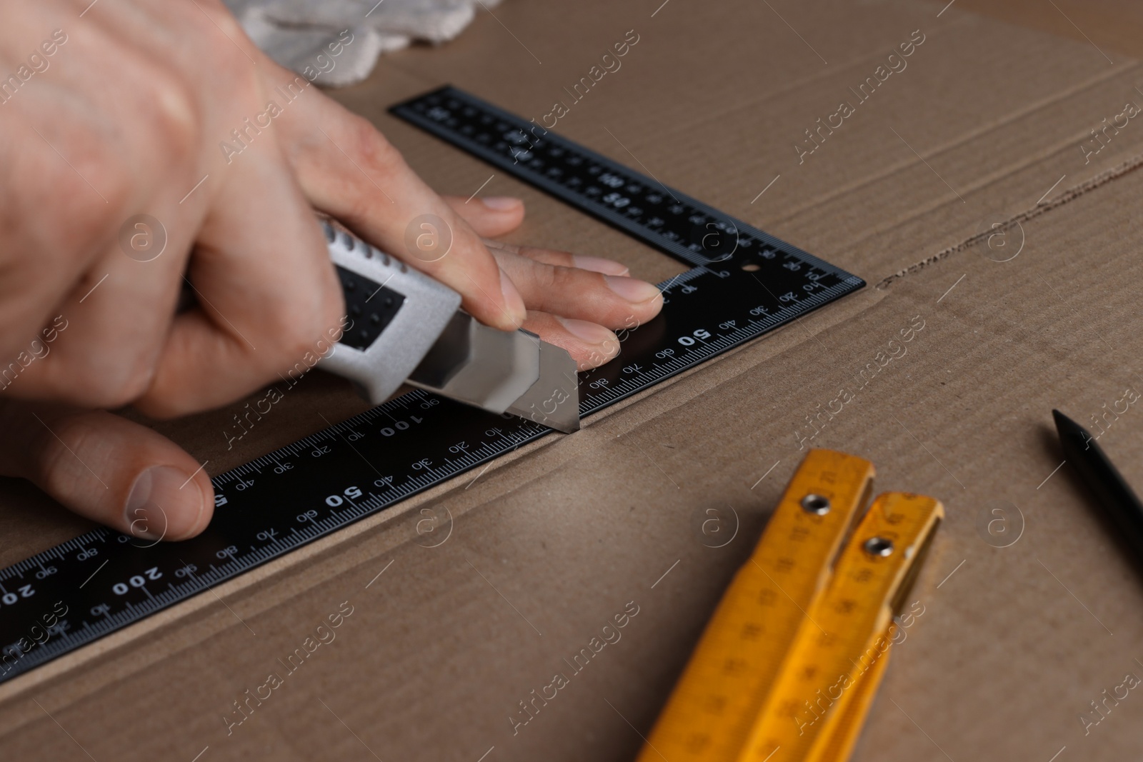 Photo of Man cutting cardboard with utility knife and ruler, closeup