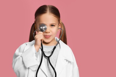 Photo of Little girl in medical uniform with stethoscope on pink background. Space for text