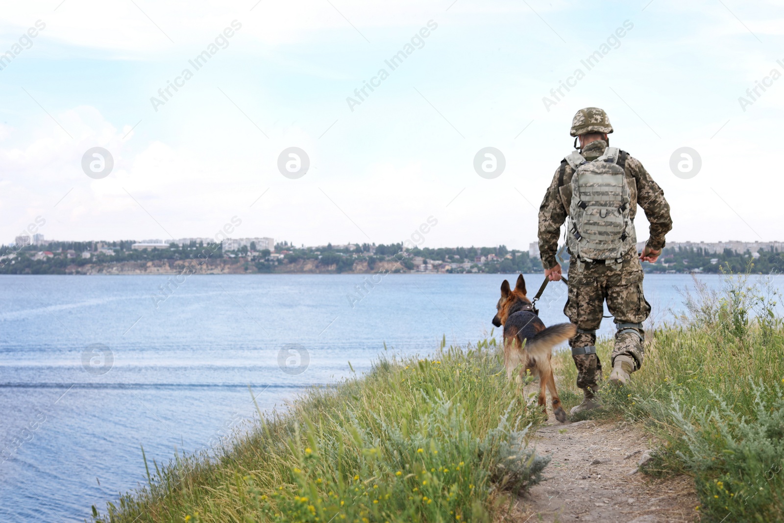 Photo of Man in military uniform with German shepherd dog near river