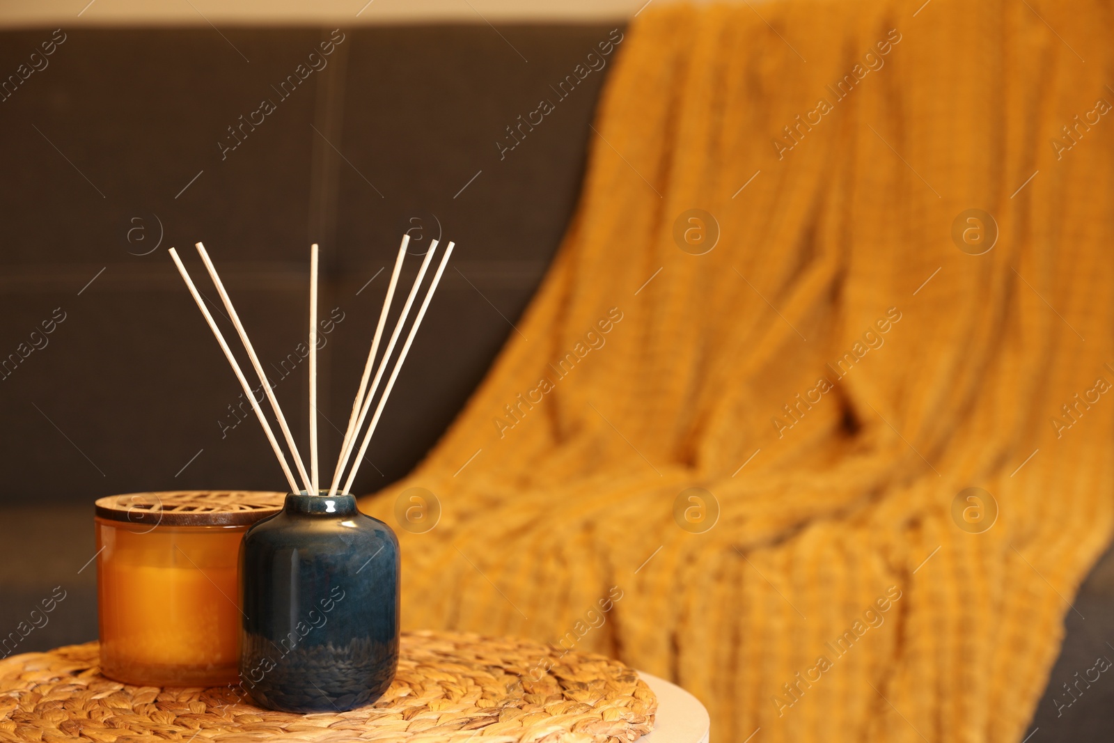 Photo of Aromatic reed air freshener and scented candle on table indoors, space for text